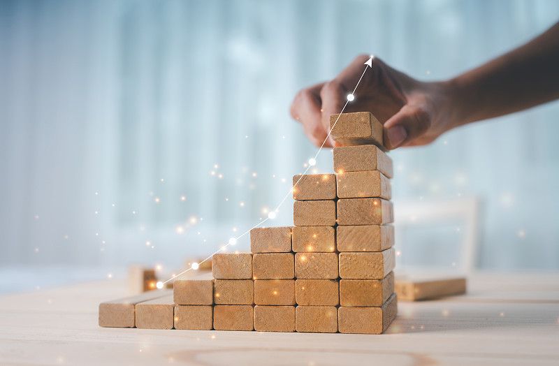 一位女商人的手正在沿着上升的图形排列木制玩具。图片下载