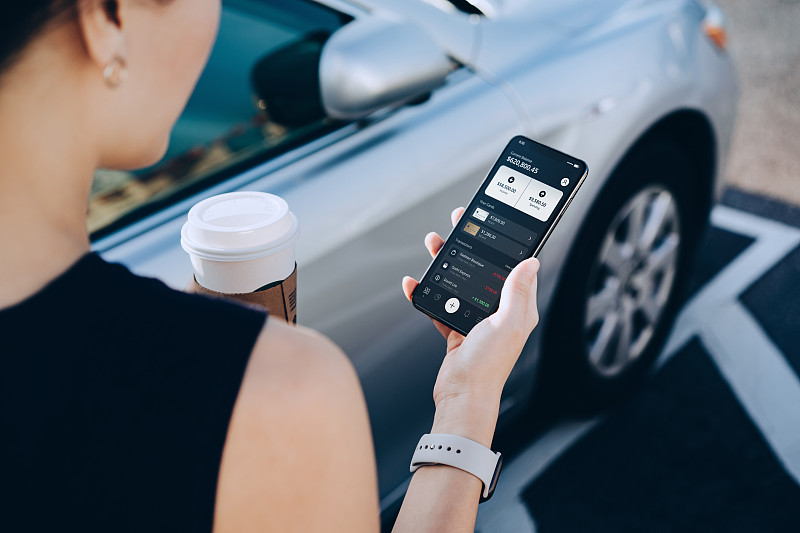 这是一位年轻的亚洲女商人,一边喝着咖啡,一边用智能手机上的移动应用管理着网上银行。转钱,付账单,查看余额,走到她的车在市中心的停车场图片下载