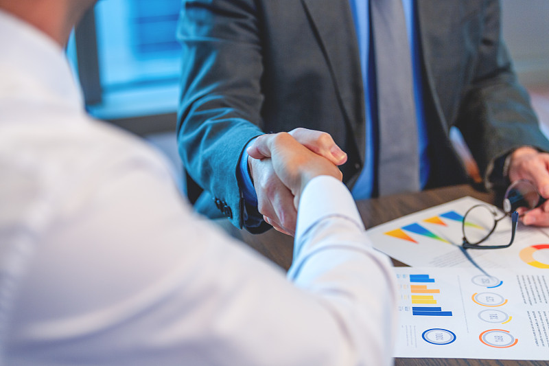 商人们握手的特写。两人都穿着职业装,有文件和一台电脑图片下载