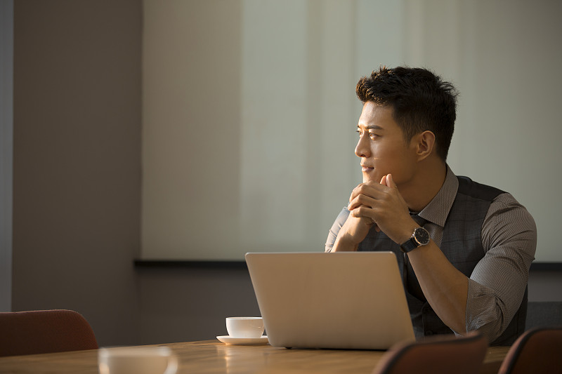 一个商务青年男子在会议室使用笔记本电脑工作思考看向窗外图片下载