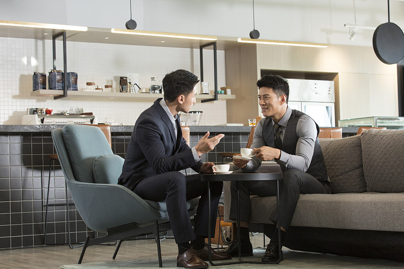 两个成功商务青年男子在酒店咖啡馆喝咖啡沟通讨论工作图片下载